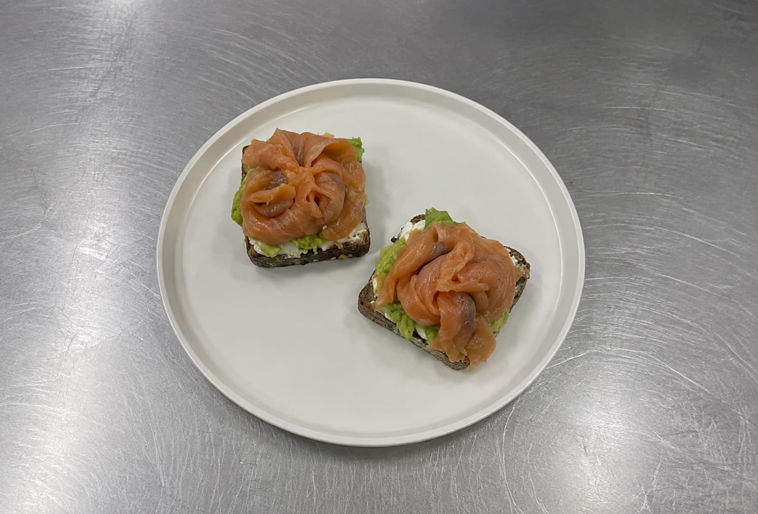 Ordinary smartphone photo of two salmon sushi bites on a white plate and steel counter